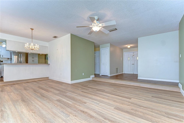 unfurnished living room featuring light wood-type flooring, visible vents, and ceiling fan with notable chandelier