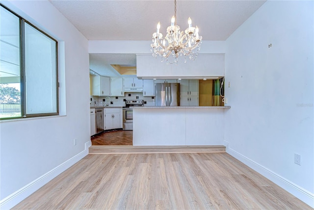 kitchen featuring light wood finished floors, a chandelier, under cabinet range hood, appliances with stainless steel finishes, and white cabinets