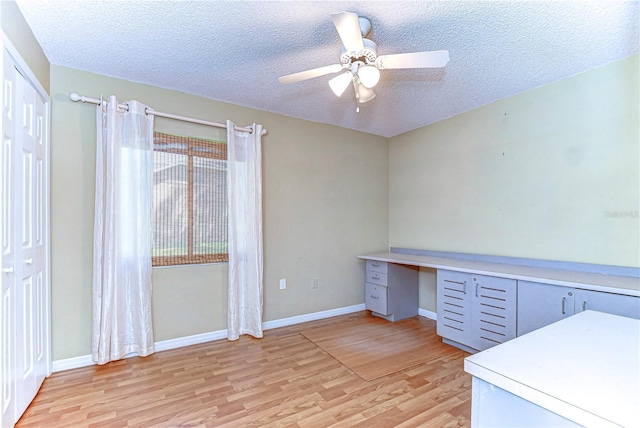 unfurnished office with light wood finished floors, baseboards, a textured ceiling, and a ceiling fan