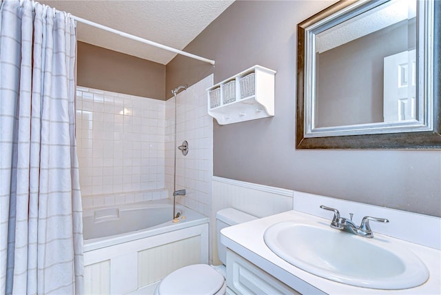 bathroom with a wainscoted wall, toilet, shower / bath combo with shower curtain, a textured ceiling, and vanity