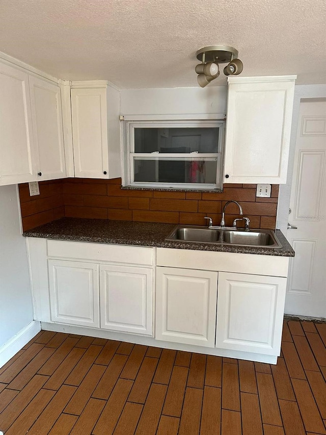 kitchen with dark countertops, dark wood-type flooring, white cabinets, and a sink