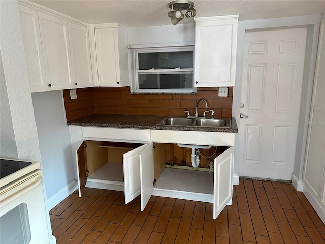 kitchen featuring a sink, white cabinetry, baseboards, decorative backsplash, and dark countertops