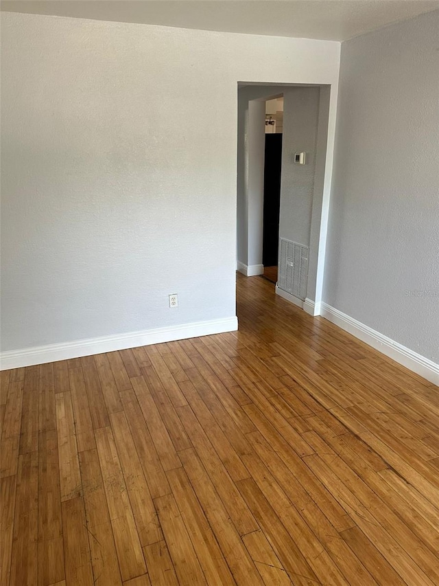 empty room with wood-type flooring, visible vents, and baseboards