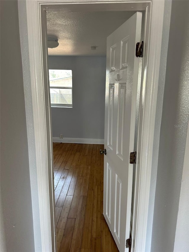 hallway with a textured ceiling, dark wood-style flooring, and baseboards