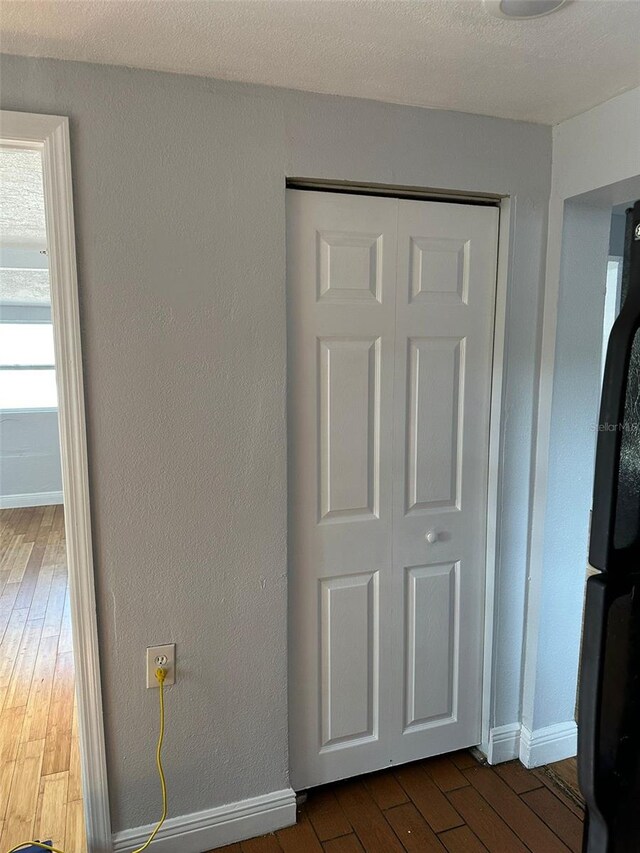 interior details with a textured wall, wood finished floors, freestanding refrigerator, and baseboards