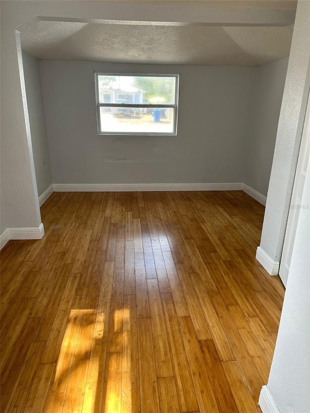 unfurnished room featuring a textured ceiling, hardwood / wood-style floors, and baseboards