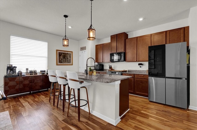 kitchen featuring a sink, stainless steel appliances, an island with sink, and wood finished floors