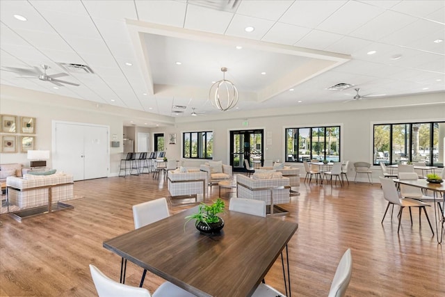 dining room with light wood-style floors, a tray ceiling, a ceiling fan, and visible vents