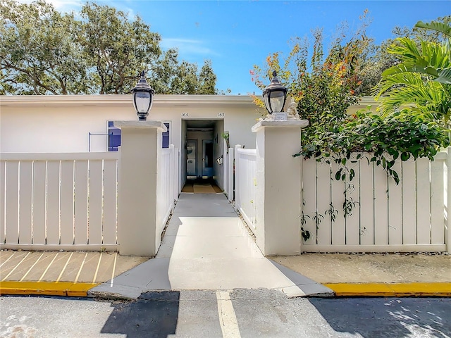 entrance to property featuring a gate, fence, and stucco siding