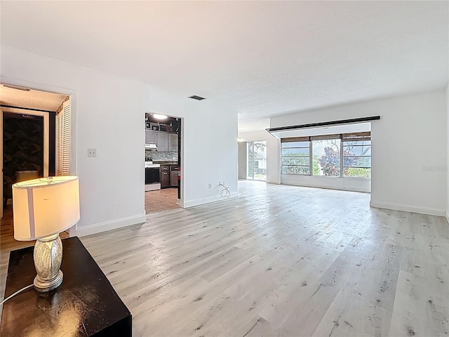 unfurnished living room featuring visible vents, baseboards, and light wood finished floors