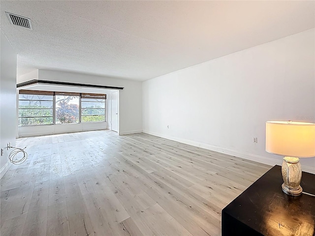 unfurnished living room featuring visible vents, baseboards, a textured ceiling, and wood finished floors