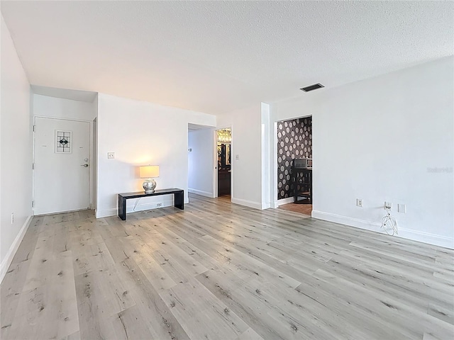 spare room featuring visible vents, light wood-style flooring, a textured ceiling, and baseboards