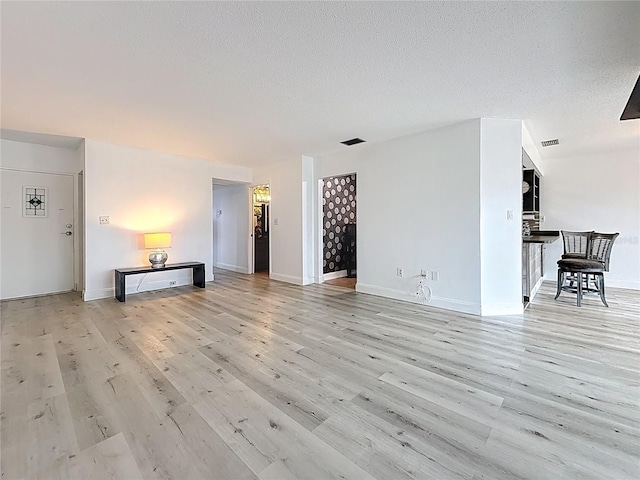 unfurnished living room with visible vents, a textured ceiling, light wood-type flooring, and baseboards