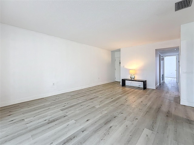 spare room featuring a textured ceiling, light wood-style floors, visible vents, and baseboards