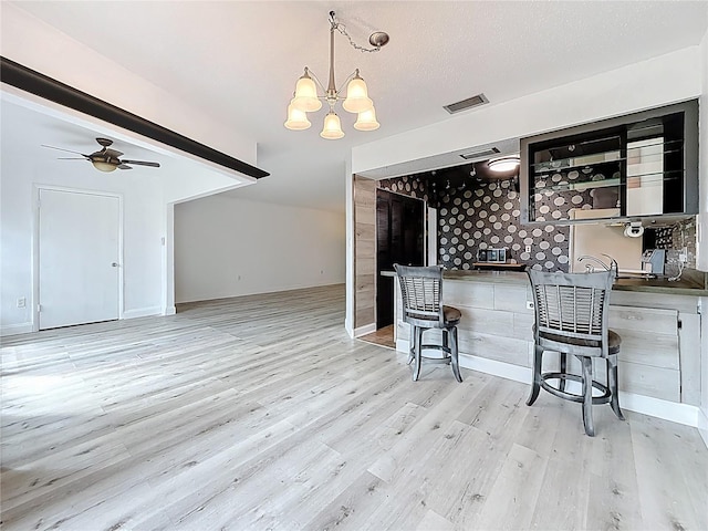 kitchen with a ceiling fan, visible vents, a kitchen bar, decorative light fixtures, and light wood-type flooring