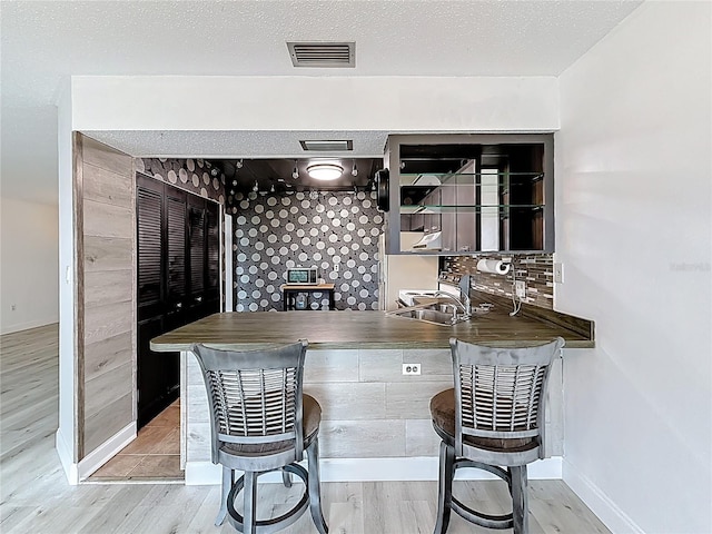 bar featuring visible vents, a sink, a textured ceiling, wood finished floors, and baseboards