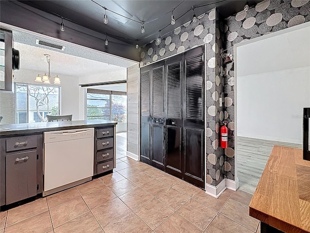 kitchen with dark countertops, visible vents, decorative light fixtures, light tile patterned floors, and white dishwasher