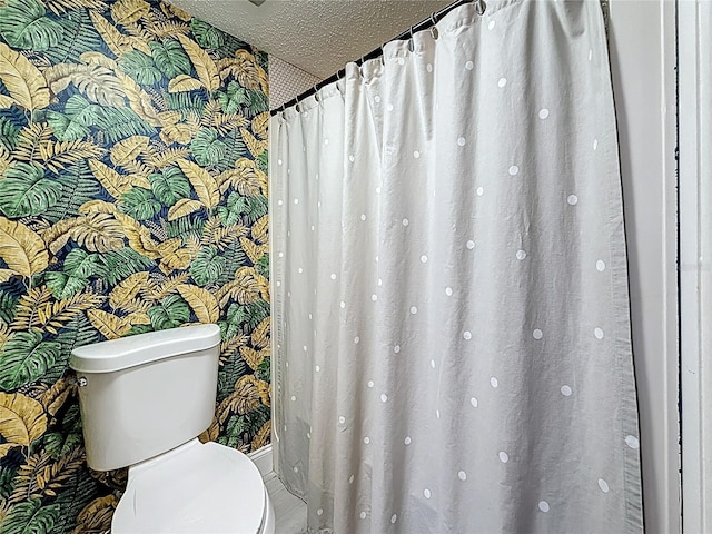 bathroom with a textured ceiling, toilet, and wallpapered walls