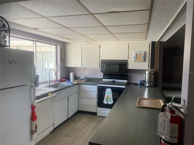 kitchen featuring white appliances, a sink, white cabinets, a paneled ceiling, and light wood-style floors