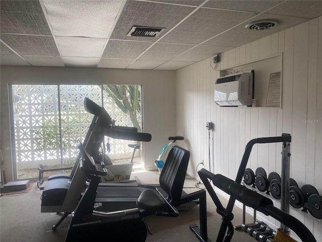 exercise room with carpet flooring, a paneled ceiling, visible vents, and a wall mounted AC