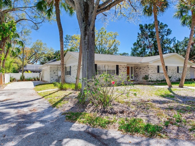 single story home featuring aphalt driveway, brick siding, an attached garage, and fence