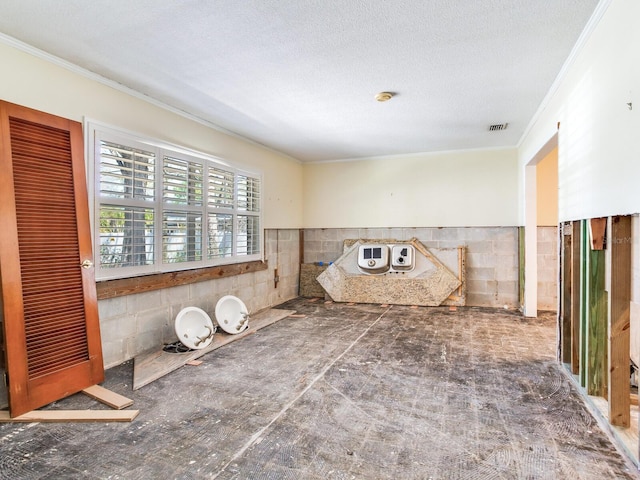 spare room featuring crown molding, concrete block wall, visible vents, and a textured ceiling