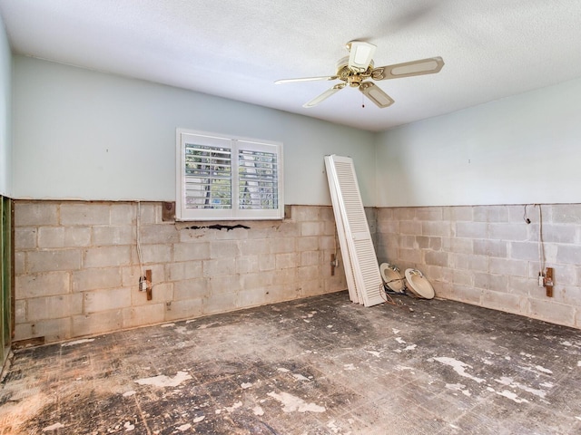 unfurnished room with a textured ceiling, ceiling fan, and concrete block wall