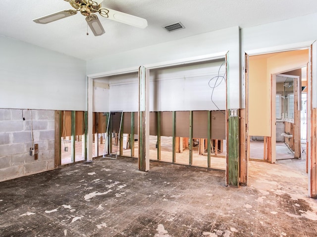 interior space featuring concrete block wall, a ceiling fan, and visible vents