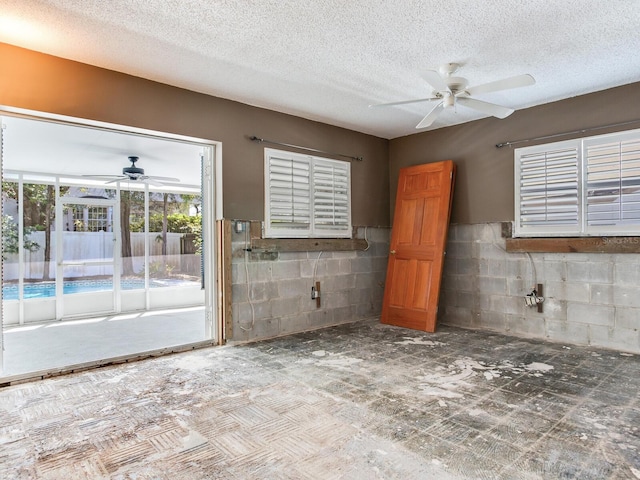 empty room featuring ceiling fan and concrete block wall