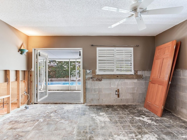 unfurnished room featuring a textured ceiling, concrete block wall, and ceiling fan