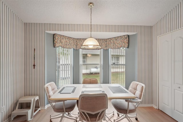 dining area with wallpapered walls, baseboards, light wood-type flooring, and a textured ceiling