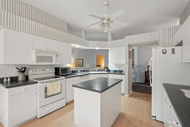 kitchen with dark countertops, a kitchen island, light wood-style flooring, white cabinets, and white appliances