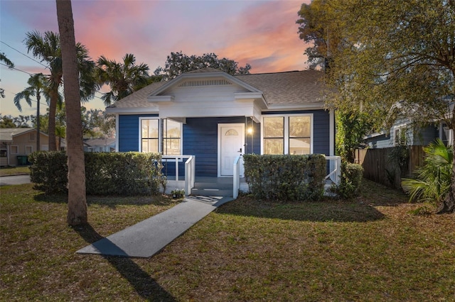 bungalow-style house with a porch, fence, a shingled roof, and a front lawn