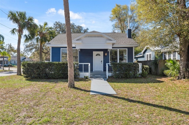 bungalow-style house with a shingled roof, a chimney, a front lawn, and fence