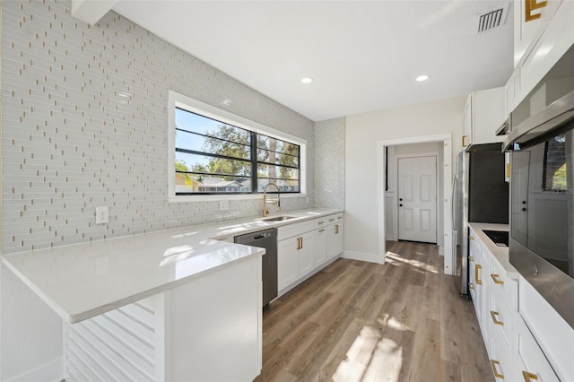 kitchen with white cabinets, decorative backsplash, a peninsula, stainless steel dishwasher, and a sink