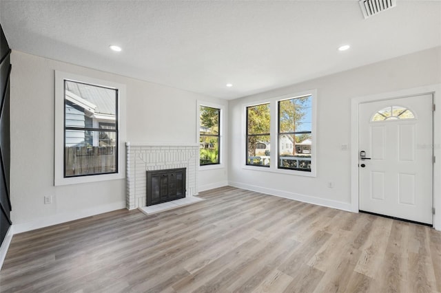 unfurnished living room with a fireplace, wood finished floors, visible vents, and baseboards