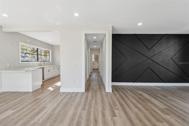 unfurnished living room featuring light wood-style floors, baseboards, a sink, and recessed lighting