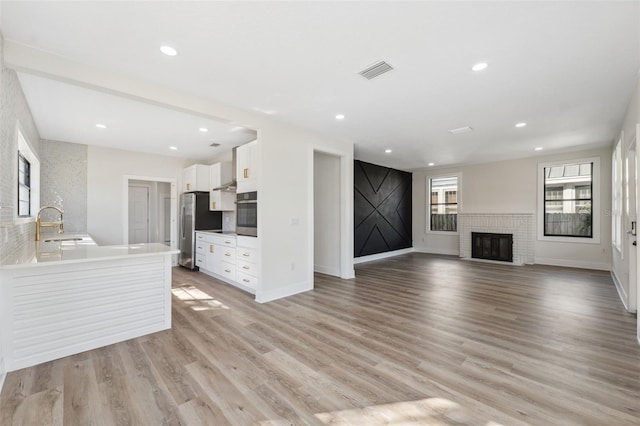 unfurnished living room featuring light wood-style flooring, a brick fireplace, visible vents, and recessed lighting