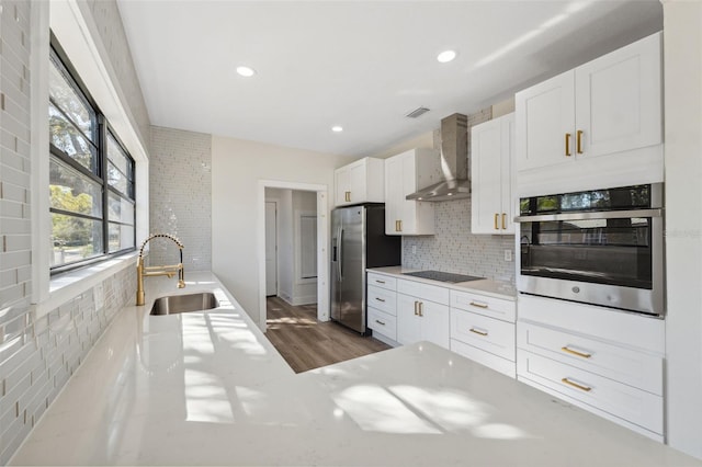 kitchen featuring tasteful backsplash, white cabinets, appliances with stainless steel finishes, wall chimney range hood, and a sink