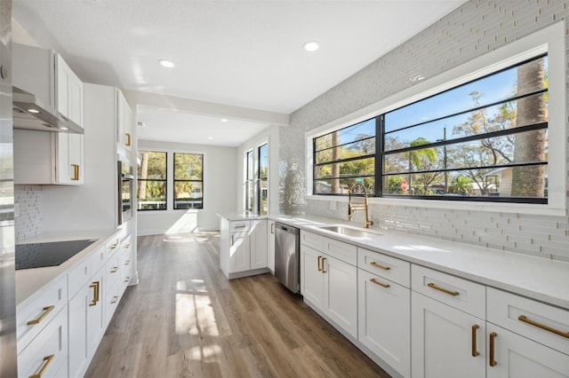 kitchen with wall chimney range hood, stainless steel appliances, light countertops, light wood-style floors, and a sink