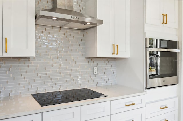 kitchen with black electric stovetop, light countertops, white cabinets, oven, and wall chimney exhaust hood