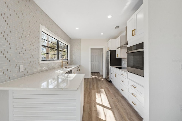 kitchen featuring light wood finished floors, tasteful backsplash, visible vents, appliances with stainless steel finishes, and white cabinetry