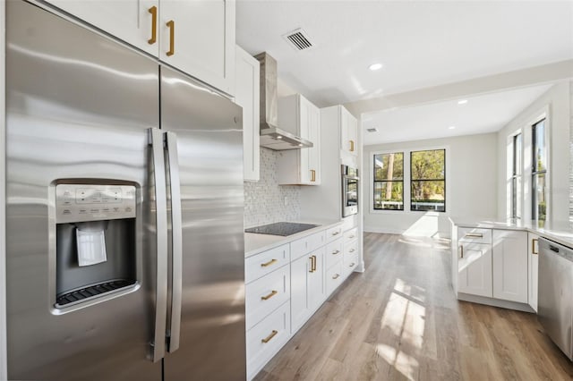 kitchen with white cabinets, appliances with stainless steel finishes, backsplash, wall chimney exhaust hood, and light wood finished floors