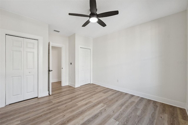 unfurnished bedroom with multiple closets, baseboards, visible vents, and light wood finished floors