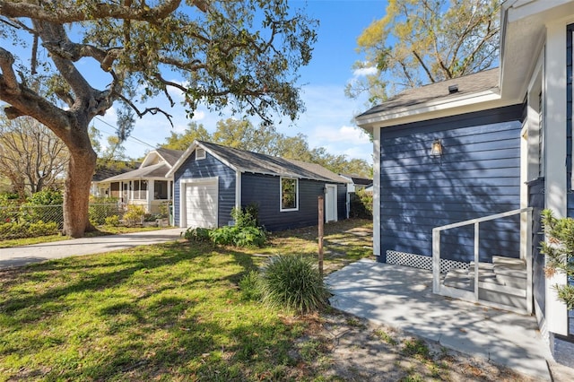 exterior space featuring a garage, an outdoor structure, fence, concrete driveway, and a front lawn