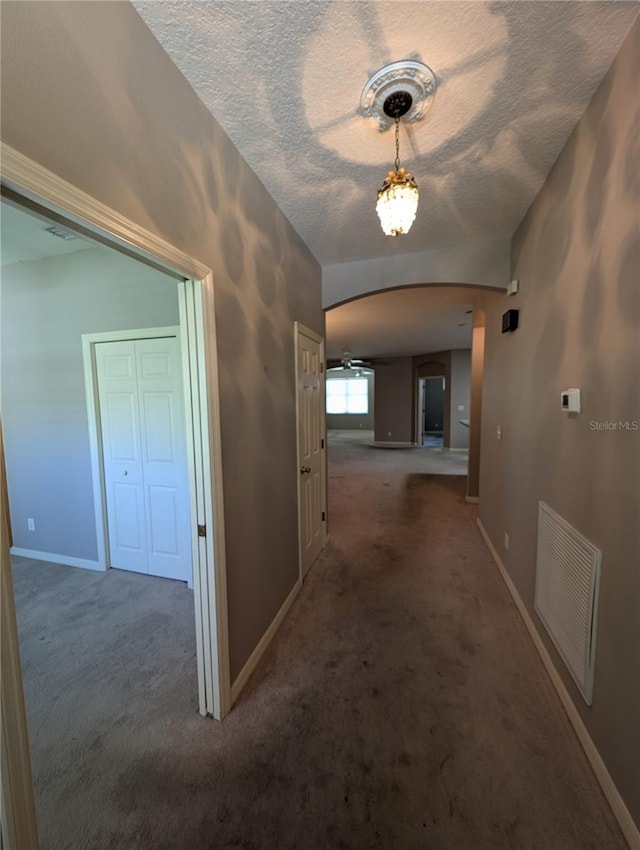 hallway with arched walkways, carpet floors, visible vents, and baseboards