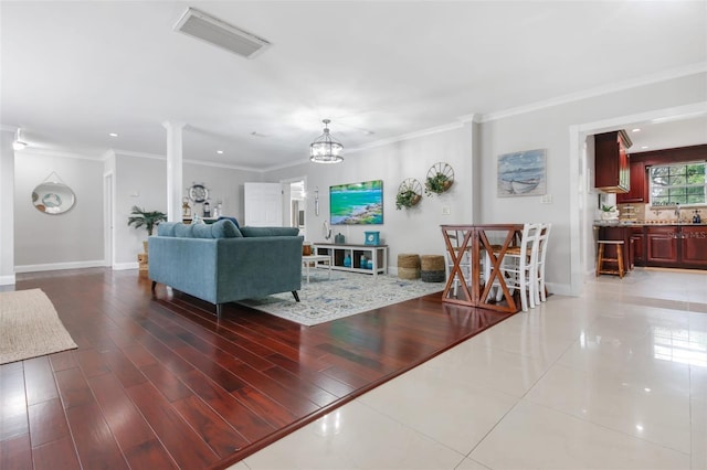 living room with crown molding, ornate columns, visible vents, wood finished floors, and baseboards