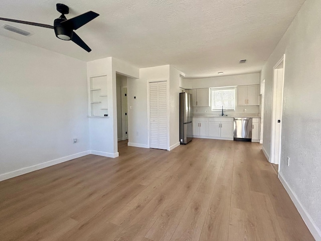 unfurnished living room with baseboards, light wood-style flooring, visible vents, and a sink