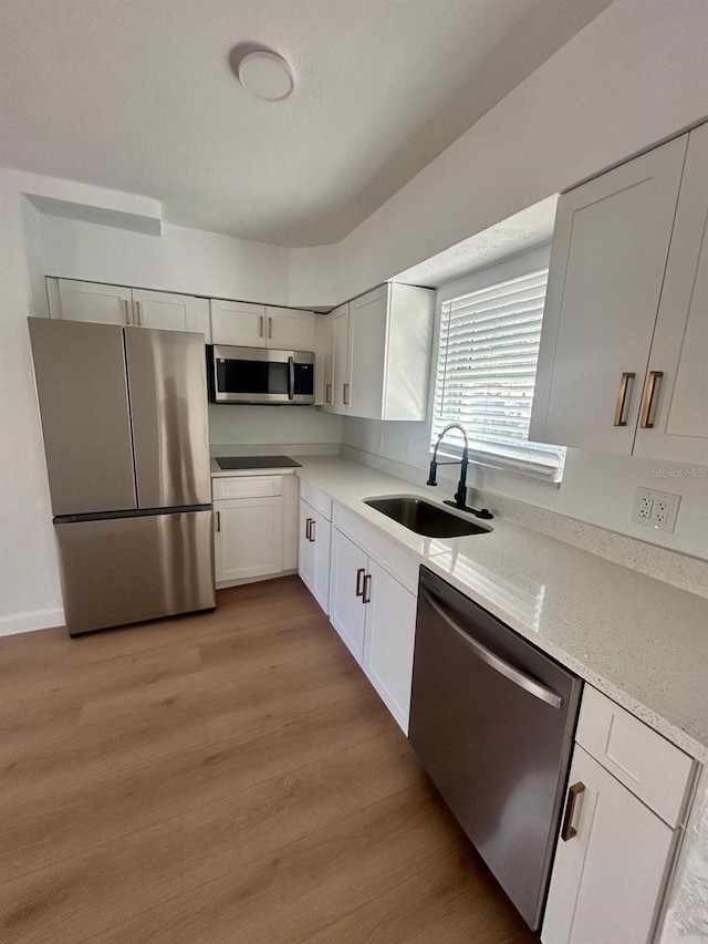 kitchen with appliances with stainless steel finishes, white cabinets, a sink, and light wood finished floors