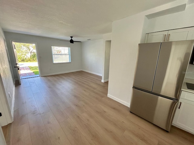 interior space featuring light wood-style flooring, baseboards, ceiling fan, and a textured ceiling